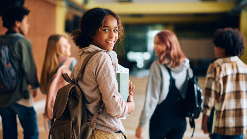 Happy black teenage girl in high school hallway looking at camera.